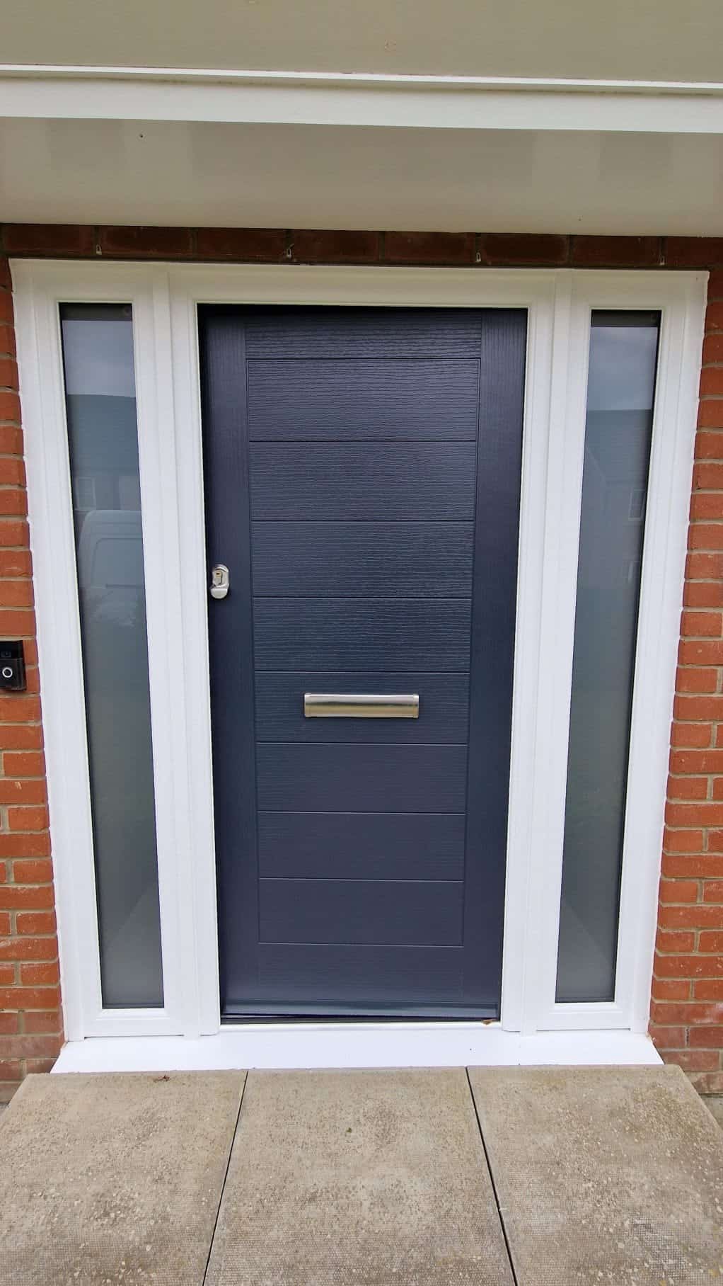 Dark blue composite replacement door in Ely with glazed side panels and brushed metal letterbox.