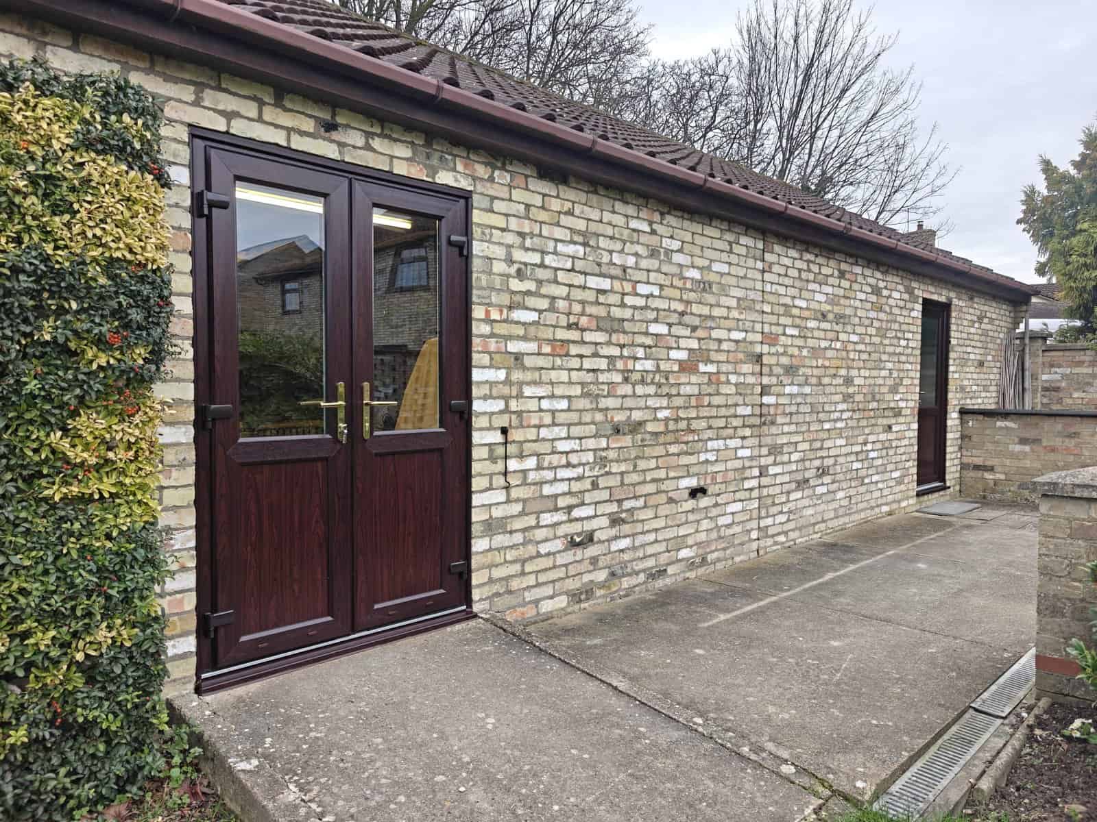 Dark wood-effect glazed replacement doors in Ely fitted to a brick residential property.