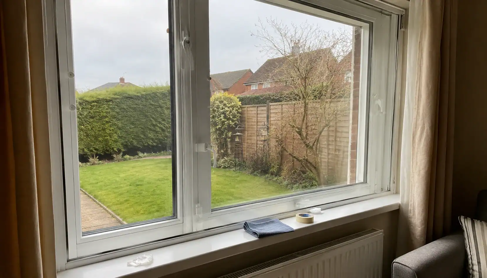 Secondary glazing in Ely fitted to a large white-framed living room window overlooking a residential garden.