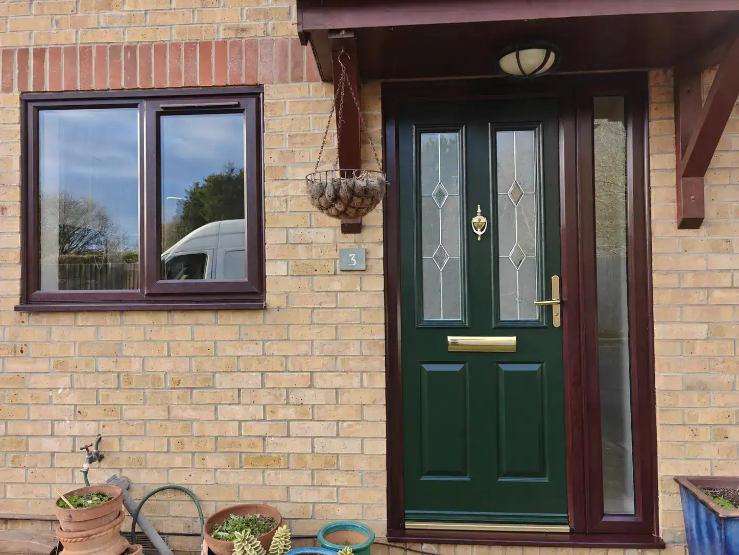 Green composite front door with decorative glazing and brass hardware fitted to a brick home in Ely.